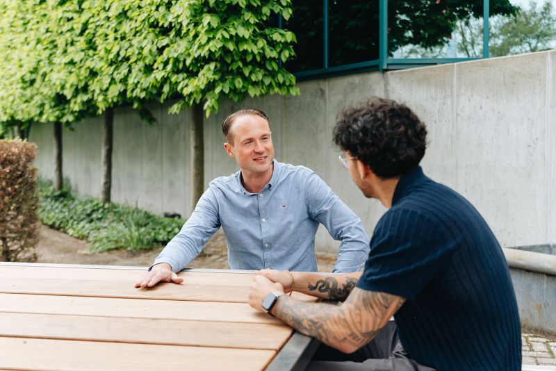 Twee medewerkers zitten buiten aan tafel